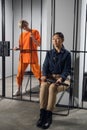 A young taskmaster in uniform sits on a chair next to the camera of a blonde criminal