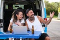 Young tattooed couple smile and talk in a laptop video call during a van trip. Royalty Free Stock Photo