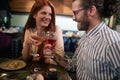 Young tattooed man with a beard drinking wine with a beautiful redhead female at romantic dinner in restaurant, toasting, looking