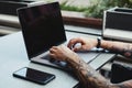 Young tattooed man working on laptop in a coffee shop. Rear view of hipster hands with tattoo busy using laptop at coworking