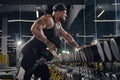 Young, tattooed, muscular man in black shorts, vest and cap. Exercising with dumbbells for training his triceps in dark Royalty Free Stock Photo