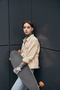 young tattooed woman holding skateboard against black