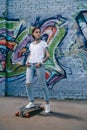 young tattooed woman standing on skateboard near wall