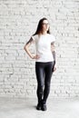 Young tattooed woman wearing blank t-shirt, standing in front of brick wall in loft.