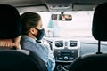 A young taxi driver woman in a black medical mask with blond hair and a jacket is driving a left-hand drive car Royalty Free Stock Photo