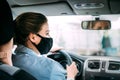 A young taxi driver woman in a black medical mask with blond hair and a jacket is driving a right-hand drive car Royalty Free Stock Photo