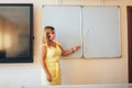 Young teacher in a medical mask holding a pointer in her hand and points to a white board, back to school, modern education, Royalty Free Stock Photo