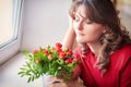 A young teacher is sad at the window at graduation. The woman at the school on farewell to students. Teacher with a bouquet of red