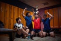 Young team players celebrating first place won, holdin golden trophy and cheering in the locker room