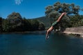 Young teen boy jumping flying and diving in the river. Clear blue sky and trees in distance as a natural background. Royalty Free Stock Photo