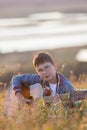 Young teen boy playing on acoustic guitar at summer field on sunset and looking to camera Royalty Free Stock Photo