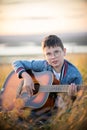 Young teen boy playing on acoustic guitar at summer field on sunset and looking to camera Royalty Free Stock Photo