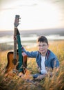 Young teen boy playing on acoustic guitar at summer field on sunset and looking to camera Royalty Free Stock Photo