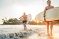 Young teen boy with a surfboard walking with his father by ocean sandy beach after surfing with beautiful sunset background. They Royalty Free Stock Photo