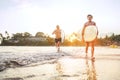 Young teen boy with a surfboard walking with his father by ocean sandy beach after surfing with beautiful sunset background. They Royalty Free Stock Photo