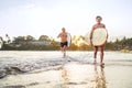 Young teen boy with a surfboard walking with his father by ocean sandy beach after surfing with beautiful sunset background. They Royalty Free Stock Photo