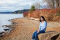 Young teen girl in blue shirt and jeans sitting along rocky lake shore Royalty Free Stock Photo