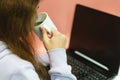 Young teen girl in home clothes at home near laptop drinking coffee during study break online. Royalty Free Stock Photo