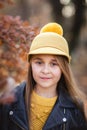 Young teen girl with long blond hair in yellow sweater, hat and leather jacket posing in the autumn park. Copy space Royalty Free Stock Photo