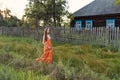 A young woman in an old-fashioned vintage sarafan dress is walking along the fence of a rustic abandoned wooden house Royalty Free Stock Photo