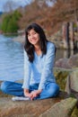 Young teen girl relaxing on large boulder along lake shore, smiling Royalty Free Stock Photo