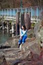 Young teen girl sitting on large boulders along lake shore, looking out over water