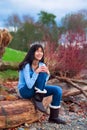 Young Teen Girl Sitting On Log Along Rocky Beach Of Lake