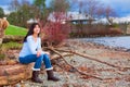 Young Teen Girl Sitting On Log Along Rocky Beach Of Lake