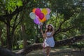 Young teen girl sitting on tree and holding balloons in hand.