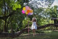 Young teen girl sitting on tree and holding balloons in hand.