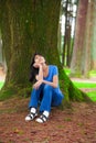 Young teen girl sitting under large pine trees, thinking Royalty Free Stock Photo