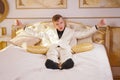 Young teen guy wearing white business suit and lying on the bed in his Golden room, stretching and yawning