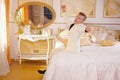 Young teen guy wearing white business suit and lying on the bed in his Golden room, stretching and yawning