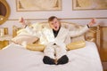 Young teen guy wearing white business suit and lying on the bed in his Golden room, stretching and yawning