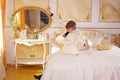 Young teen guy wearing white business suit and lying on the bed in his Golden room, stretching and yawning