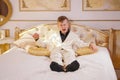 Young teen guy wearing white business suit and lying on the bed in his Golden room, stretching and yawning