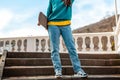 A young teen holding a skateboard behind her back is standing on the steps. Bottom view. Close up. Concept of sports lifestyle and