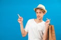 Young teen man points finger aside and holding paper bag in hand isolated on blue. Friendly well-looking boy paying your attention Royalty Free Stock Photo