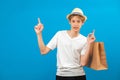 Young teen man points finger aside and holding paper bag in hand isolated on blue. Friendly well-looking boy paying your attention Royalty Free Stock Photo