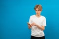 Young teen using mobile phone isolated by blue background, guy texting online, scrolling news feed, web surfing on the mobile