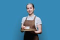 Young teenage female waitress holding tray with cup of coffee, on blue background