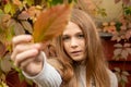 Young teenage girl ginger with freckles with autumn leaves in hand and autumn yellow and red garden background. seasons concept.