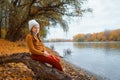 a young teenage girl posing in an autumn forest, sitting on a tree by the river bank, beautiful nature and bright yellow leaves Royalty Free Stock Photo