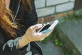 A young teenage girl is sitting outside on the street and holding a cell phone with a blank screen in her hands. Mobile phone in h Royalty Free Stock Photo