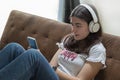 young teenage girl sitting on a sofa with her feet on the table listening to cell phone music with white headphones Royalty Free Stock Photo