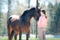 Young teenage girl standing with her favorite brown horse.