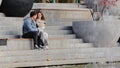 Young teenage married couple lovers caucasian family sit on urban stairs in park wear blanket hugging cuddle closer talk Royalty Free Stock Photo