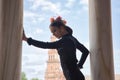 Young teenage woman with black dance dress and pink carnations in her hair, doing flamenco pose leaning on a column. Flamenco