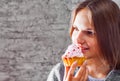 Young teenager brunette girl with long hair eating cream cake on gray wall background Royalty Free Stock Photo