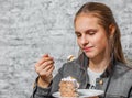 Young teenager brunette girl with long hair eating slice cake dessert on gray wall background Royalty Free Stock Photo